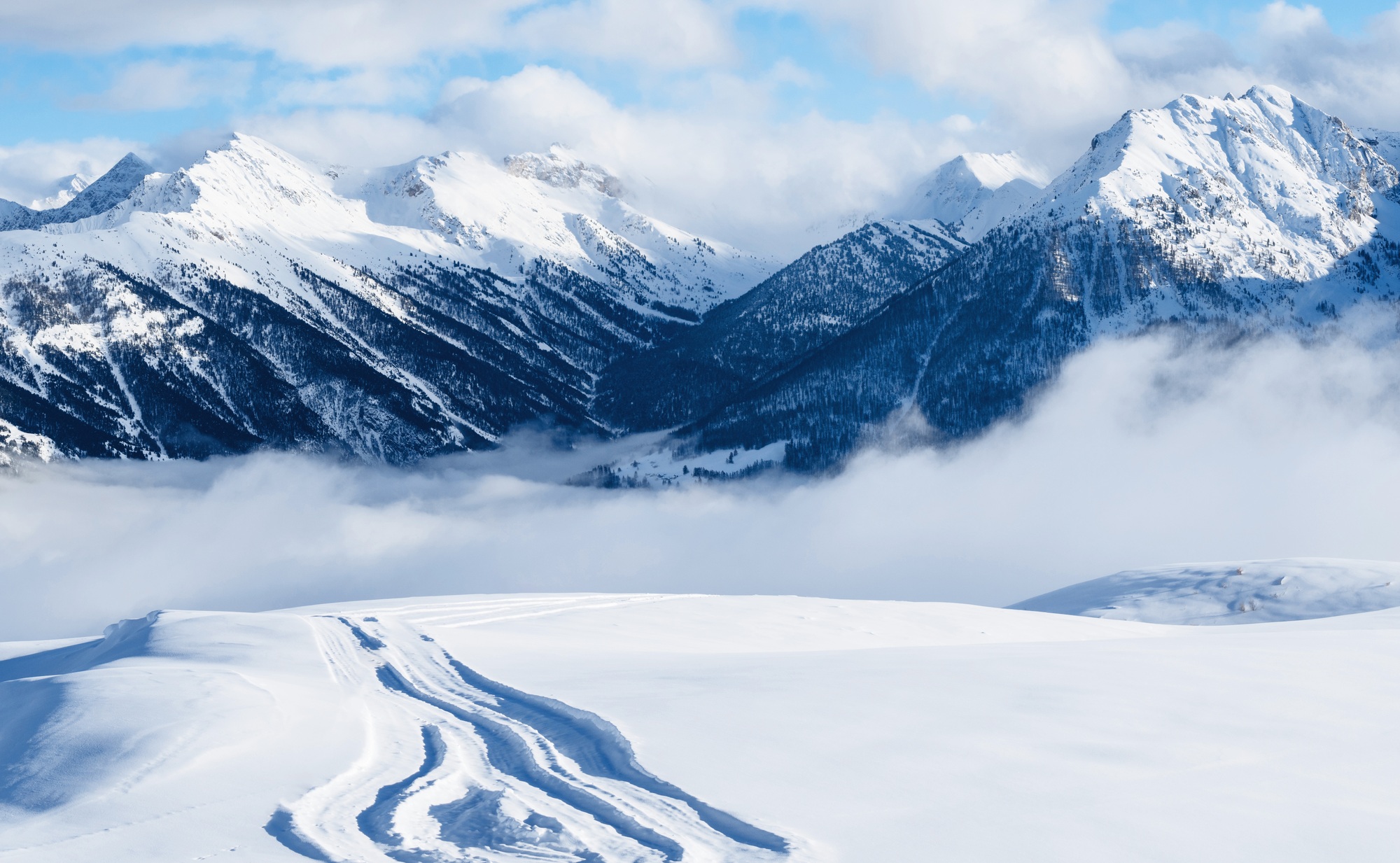 Mountain ski resort. Snowcat trail on snow slope. Snowy mountains. Ski resort landscape on clear